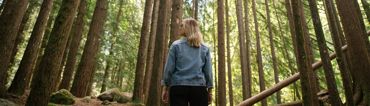 A woman standing in the woods looking up at the trees