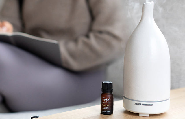 Persons sitting cross legged in the background, and diffuser and diffuser blend on a table