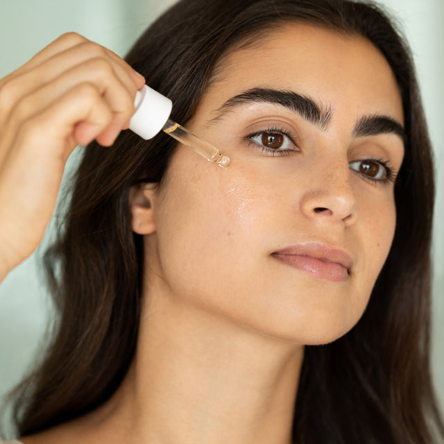 Person applying calm-o-mile face oil on their face