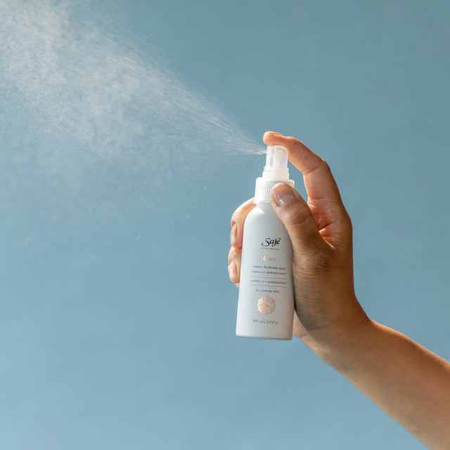 Person spraying deodorant on blue background