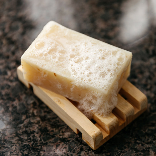 Lemongrass Sass with bubbles after getting wet, on a wooden soap holder on top of a granite countertop